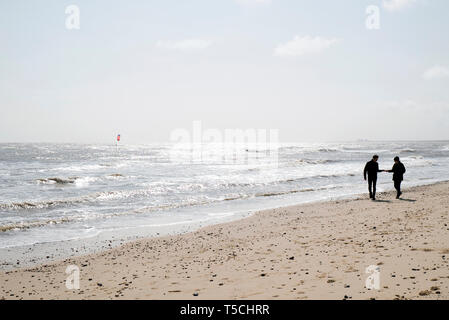 Un couple en train de marcher sur la plage dans le Suffolk AVEC UN Kite Surfer dans la distance Banque D'Images