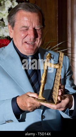 24 avril 2019, Basse-Saxe, Hanovre : l'ancien chancelier allemand Gerhard Schröder (SPD) est présenté avec une œuvre d'art lors d'une réception de la ville de Hanovre, pour marquer son 75e anniversaire dans la nouvelle mairie. ronzeskulptur par le sculpteur Siegfried Neuenhausen. La sculpture en bronze par le sculpteur Siegfried Neuenhausen, qui montre un homme en face d'une clôture, avait pour but de nous rappeler comment Schröder, en tant que jeune député après une soirée pub, secoué la clôture de la chancellerie de Bonn avec les mots 'Je veux aller là-bas". Photo : Julian Stratenschulte/dpa Banque D'Images