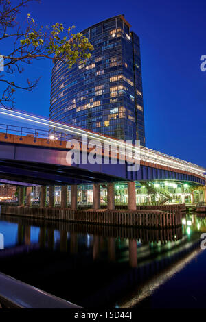 Vue nocturne de West India Quay Station, Canary Wharf, Londres, avec train de voyageurs passant par le pont et laissant un sentier flou de ses lumières Banque D'Images