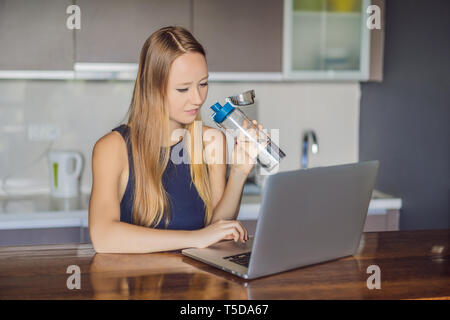 Fille assoiffée boit de l'eau, utilise un ordinateur portable pour le blogging en réseaux, montres, film connecté à internet sans fil. Femme se lit l'actualité des site web Banque D'Images