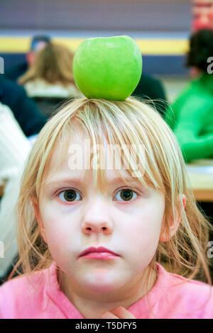 Notion de droit d'une mignonne petite fille de six ans, l'équilibre entre une pomme sur sa tête et regardant attentivement à l'appareil photo Banque D'Images