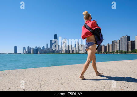 Jeune femme blonde en bikini blanc marche sur Chicago Lakefront Trail avec l'horizon de Chicago dans l'arrière-plan Banque D'Images