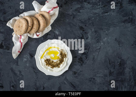 Labneh (labaneh) blanc doux moyen-orientale fromage de chèvre à l'huile d'olive, olives , za'atar , citron, avec du pain pita sur la plaque en bois noir, flatl Banque D'Images