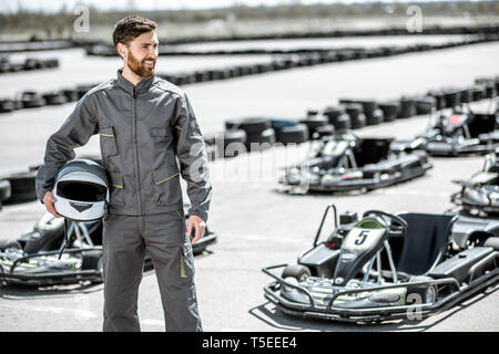 Portrait d'un heureux et excité racer dans les vêtements de sport comité permanent sur la piste avec des karts en plein air Banque D'Images