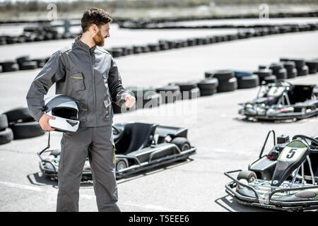 Portrait d'un heureux et excité racer dans les vêtements de sport comité permanent sur la piste avec des karts en plein air Banque D'Images