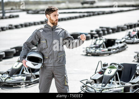 Portrait d'un heureux et excité racer dans les vêtements de sport comité permanent sur la piste avec des karts en plein air Banque D'Images