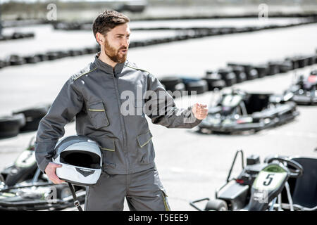 Portrait d'un heureux et excité racer dans les vêtements de sport comité permanent sur la piste avec des karts en plein air Banque D'Images