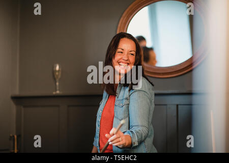 Portrait of a smiling woman, elle se tient à l'intérieur avec une baguette de billard et de rire.