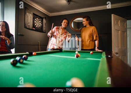 Petit groupe d'amies de jouer à un jeu de billard dans une salle de jeux dans une maison. Banque D'Images