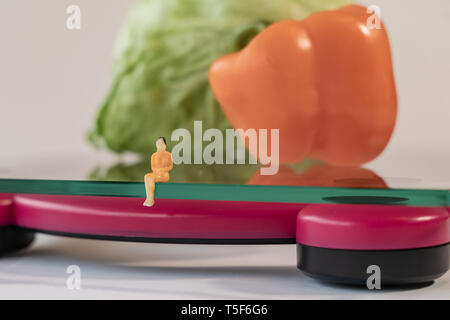 Femme miniature figure l'emplacement de l'électronique numérique balance de salle pour les poids de corps humain. Des légumes frais à faible profondeur de champ background Banque D'Images