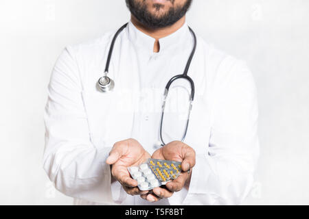 Beau jeune médecin dans une robe blanche avec un stéthoscope détient sur une main tendue un comprimés en plaquettes thermoformées. Banque D'Images