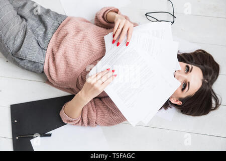 Une belle femme se trouve sur le sol au milieu des papiers et documents, la jeune fille sourit et se détend pendant freelancer une pause du travail Banque D'Images