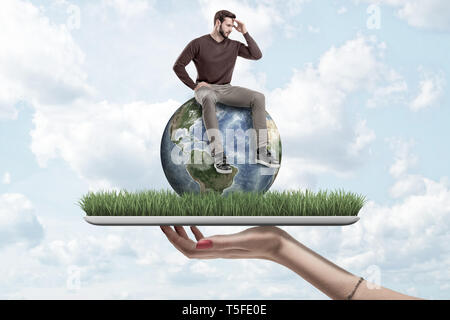 Femme Homme petite main tenant dans les tenues de assis sur la terre globe on Green grass modèle avec fond de ciel bleu