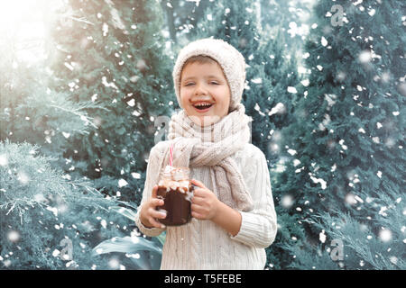 Adorable petit garçon en pull-over chaud et avec pot Mason de chocolat chaud sur jour de neige Banque D'Images