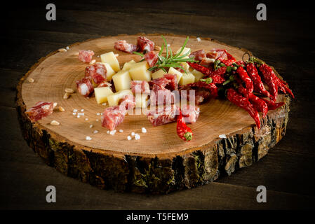 Les dés de salami et de fromage sur une plaque de bois avec un tronc d'arbre avec les piments et écrit Banque D'Images