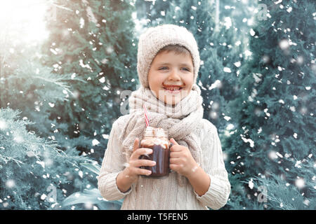 Adorable petit garçon en pull-over chaud et avec pot Mason de chocolat chaud sur jour de neige Banque D'Images