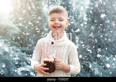 Adorable petit garçon en pull-over chaud et avec pot Mason de chocolat chaud sur jour de neige Banque D'Images