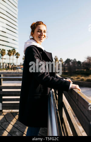 Portrait of smiling young woman leaning against a fence Banque D'Images