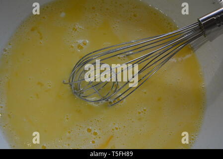 Fouet en métal de cuisine pour pétrir et battre dans l'orteil avec des œufs fouettés, du sucre et du yaourt. Banque D'Images