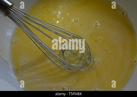 Fouet en métal de cuisine pour pétrir et battre dans l'orteil avec des œufs fouettés, du sucre et du yaourt. Banque D'Images