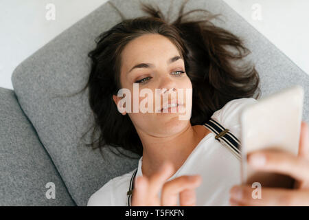 Woman lying on couch, using smartphone Banque D'Images