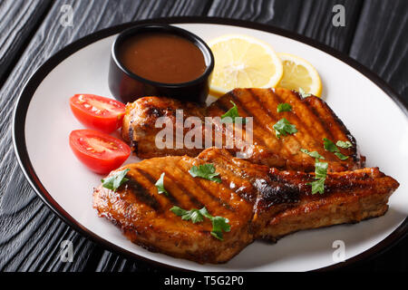 Steak de porc grillé fraîchement préparé avec sauce tamarin, citron et tomates fraîches close-up sur une plaque sur la table horizontale. Banque D'Images