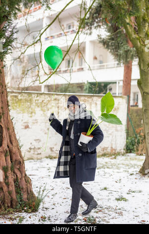 Smiling mature man avec ballon vert et plante en pot en hiver Banque D'Images