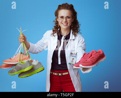 Femme médecin en bue chemise, pantalon rouge et blanc robe médical donnant une paire de chaussures de conditionnement physique tout en maintenant banc d'autres baskets dans un autre ha Banque D'Images