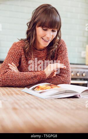 Young woman in kitchen, reading book Banque D'Images