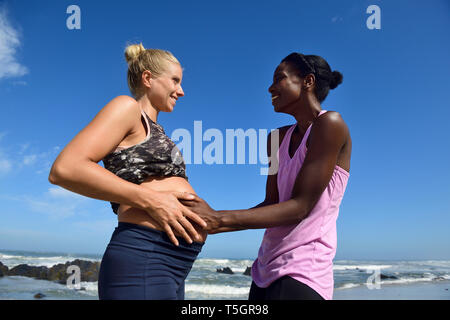 Happy woman touching belly of pregnant friend sur la plage Banque D'Images