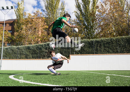 Football player kicking ball déterminé sur terrain overjumping player sur le sol Banque D'Images