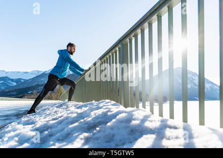 L'Allemagne, la Bavière, l'homme sportif s'étendant en hiver sur bridge railing Banque D'Images