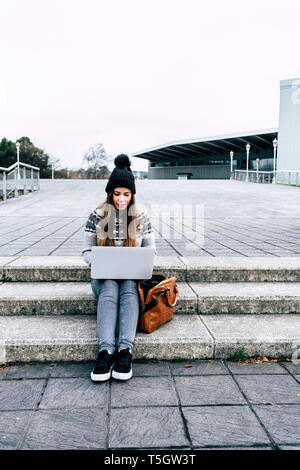 Jeune femme assise à l'extérieur dans les escaliers à l'aide d'ordinateur portable Banque D'Images