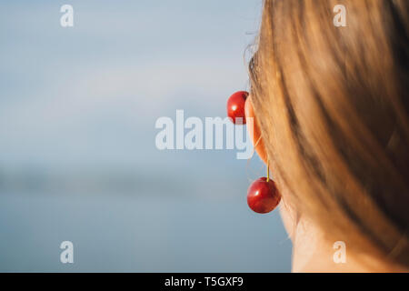 Vue arrière de jeune femme portant cerises sur l'oreille, close-up Banque D'Images