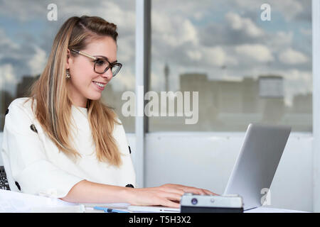 Smiling young businesswoman working on laptop in office Banque D'Images