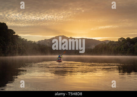 Seule une pagaie de kayak rivière encore au lever du soleil, à travers les montagnes et la forêt tropicale avec de beaux reflets dans l'eau Banque D'Images