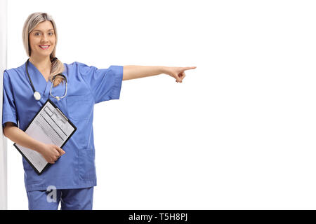 Jeune infirmière avec un presse-papiers appuyé contre un mur et de pointage isolé sur fond blanc Banque D'Images