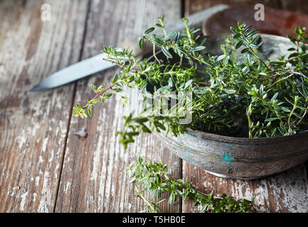 Brins de thym frais aromatique dans un vieux bol de céramique sur une table de cuisine en bois vintage usé avec couteau et copy space Banque D'Images