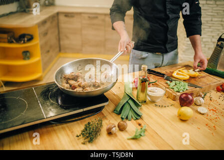 Male chef cooking meat avec vetables dans la poêle sur la cuisine. Banque D'Images