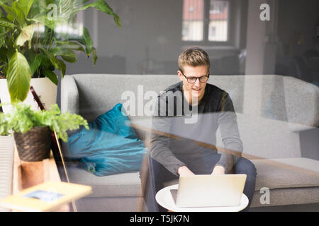 Young man sitting on couch using laptop Banque D'Images