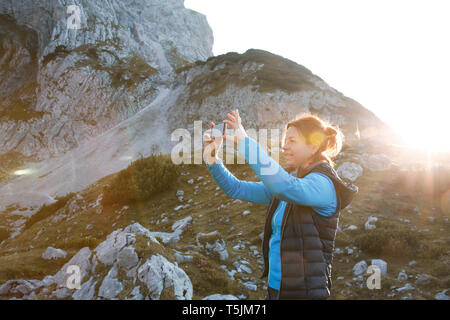 Autriche, Tyrol, woman taking cell phone photo dans mountainscape au coucher du soleil Banque D'Images