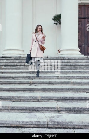 L'Autriche, Vienne, young businesswoman walking en bas à la recherche de téléphone cellulaire Banque D'Images