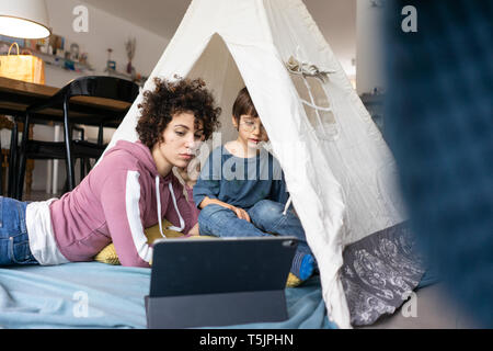 Mère et fils couché dans jouer tente, regarder la vidéo sur tablette Banque D'Images