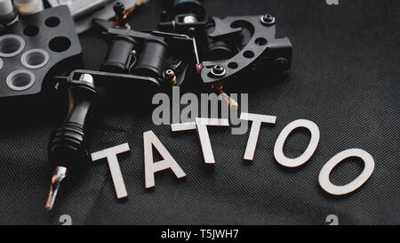 Accessoires de tatouage tatouage avec l'inscription de lettres en bois sur un fond noir. Banque D'Images