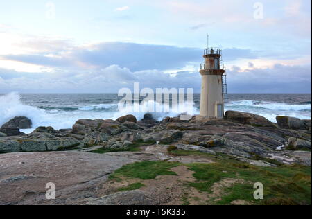 Vieux phare et les vagues se briser contre les rochers avec le coucher du soleil la lumière. Muxia, l'Espagne. Banque D'Images