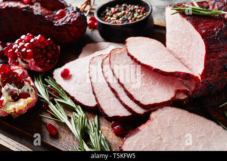 Close-up of barbecue filet de porc fumé en tranches sur une planche à découper en bois grossier avec des graines de poivre, grenat, vue d'en haut Banque D'Images