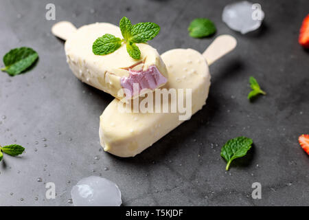 Glace à la fraise stick recouvert de chocolat blanc sur noir table de marbre Banque D'Images