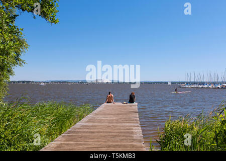 Couple sitting on jetty au lac Steinhude / Steinhuder Meer en été, Mardorf, Basse-saxe / Niedersachsen, Allemagne Banque D'Images
