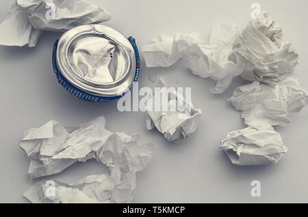 Comprimé écrasé l'aluminium peut d'une boisson gazeuse avec des feuilles de papier froissé. La pollution, les déchets, l'écologie. Banque D'Images