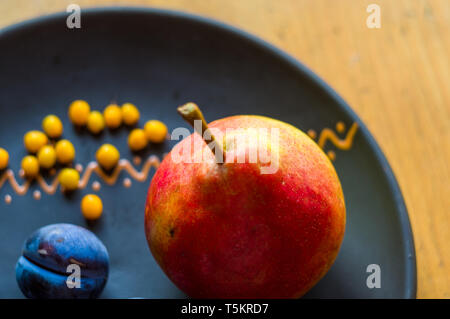 Still Life - prunes juteuses, grand bleu, de poire mûre et de petits fruits de l'argousier dans une plaque en céramique sur un fond de bois, close-up Banque D'Images